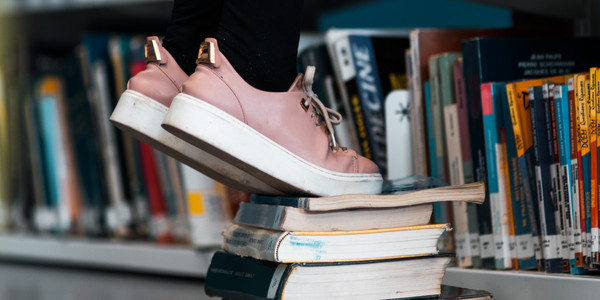 Füße auf Zehenspitzen auf einem Buchstapel um höher reichen zu können